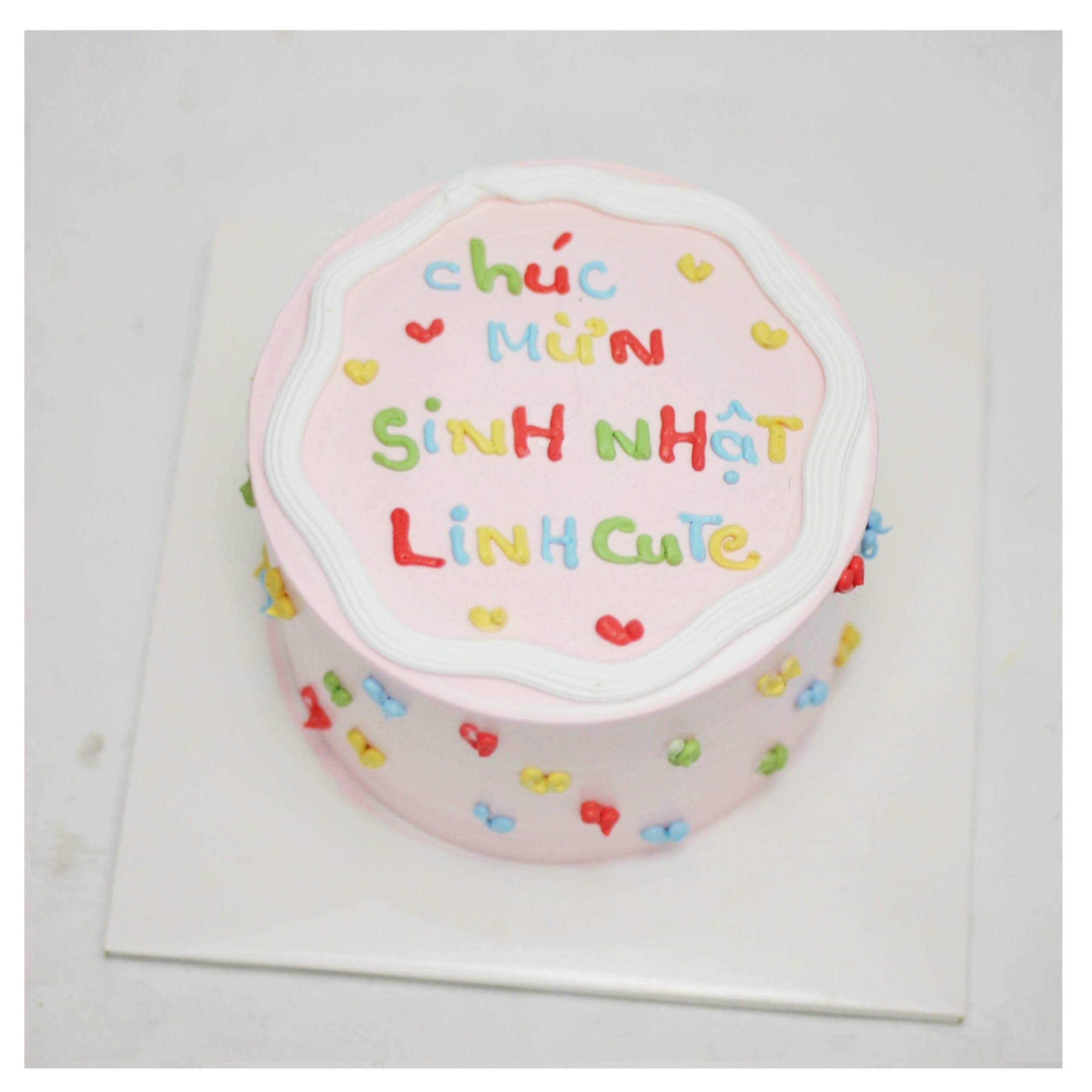 Bánh kem màu hồng trang trí chữ nhiều màu